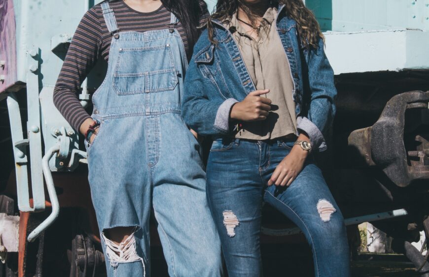 two women standing side by side wearing denim dungarees and jacket